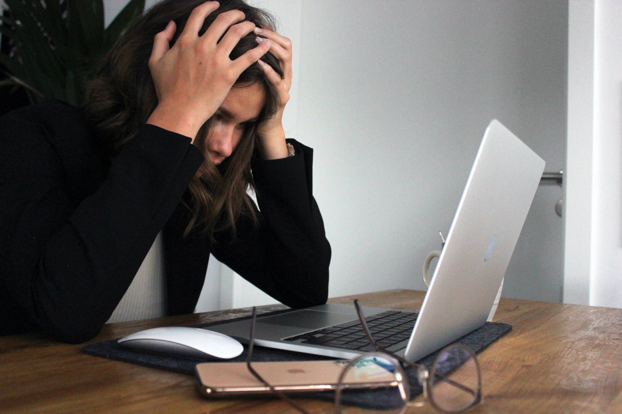 Woman at computer with hands on her head, looks concerned and stressed.